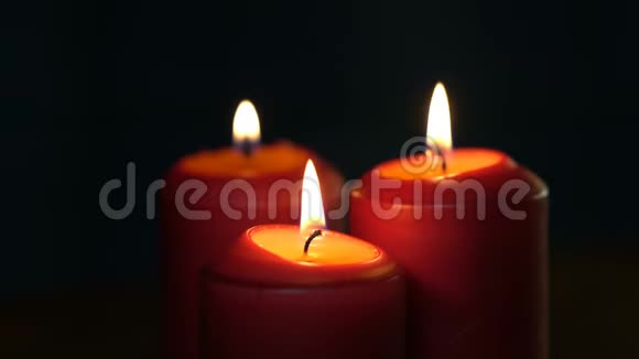 三支厚厚的红色圣诞蜡烛在黑色背景上燃烧视频的预览图
