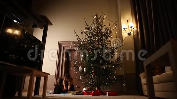 妈妈和她的女儿一起在他们家的客厅的树下开了一份圣诞礼物视频的预览图