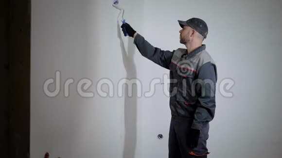 专业油漆工穿着工作制服帽子是用白色滚筒粉刷墙壁侧视视频的预览图
