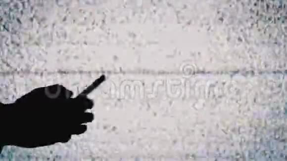 一只手拿着智能手机在电视屏幕背景上的剪影带有白色的静态噪音视频的预览图