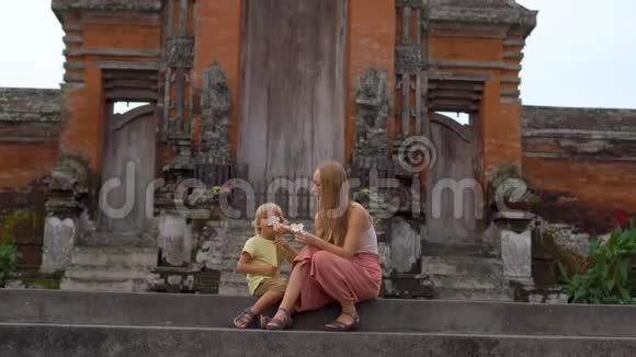 一名年轻女子和她的儿子坐在巴厘岛的塔曼阿云寺的楼梯上视频的预览图