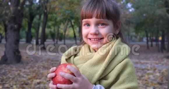 秋天漂亮的女孩子微笑着在外面的黄色树叶的背景上咬苹果视频的预览图