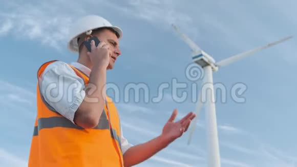 男工程师在风力涡轮机附近投射工作打个电话晴天和云彩他穿着衣服视频的预览图