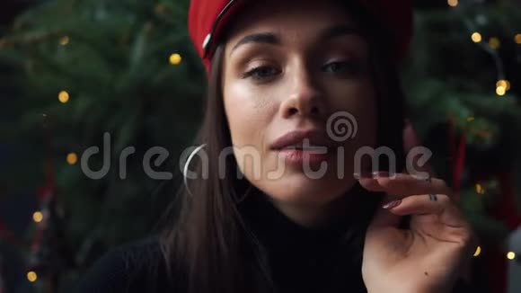 可爱的模特在圣诞树前戴着红色冬帽摆姿势视频的预览图