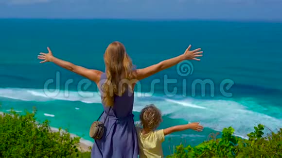 一个年轻的女人和她的儿子站在悬崖边看着海洋的慢镜头苏鲁班和恩阳视频的预览图