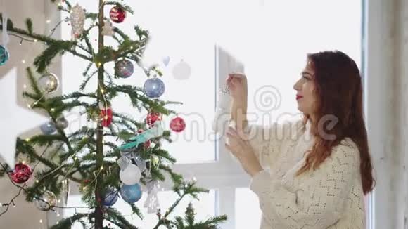 美丽的红发女人在窗边用玩具装饰圣诞树慢动作3840x2160视频的预览图