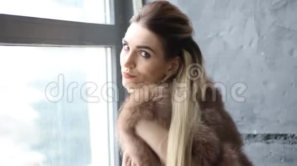 一个穿着毛皮外套的漂亮女人站在窗边时尚和风格视频的预览图