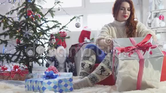 年轻漂亮的红发女人在圣诞树旁打开一个礼品盒慢动作3840x2160视频的预览图