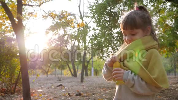 女孩子吹肥皂泡在背景树上的秋天公园里微笑视频的预览图