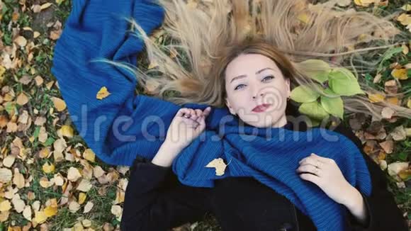 俯瞰秋天美丽的金发女人躺在树叶上慢动作3840x2160视频的预览图