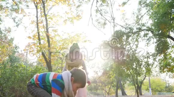 快乐的孩子在大自然中玩背光游戏在秋天公园里把黄叶扔到空中视频的预览图