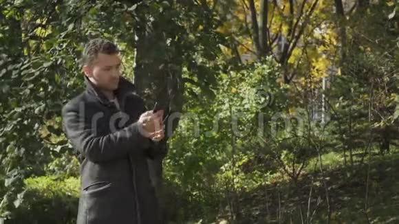 穿外套的年轻人在公园的智能手机上搜索网络信号视频的预览图