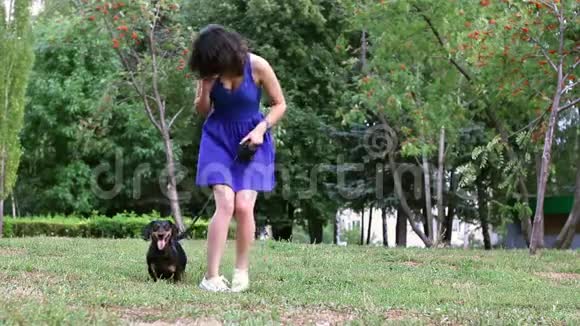 年轻女子在公园里和狗狗玩在手机上聊天视频的预览图