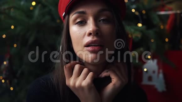 可爱的模特在圣诞树前戴着红色冬帽摆姿势视频的预览图