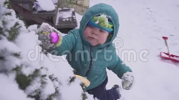 男孩孩子躺在圣诞树附近的雪上在户外玩装饰视频的预览图