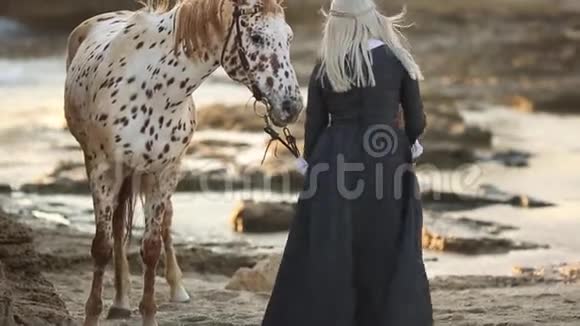 对马的治疗妈妈和女儿穿着优雅的衣服带着美丽的斑斑马走在岩石海岸上视频的预览图