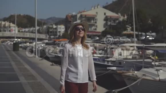 戴着帽子戴着太阳镜的漂亮女孩在美丽的大自然的背景下漫步在码头上视频的预览图