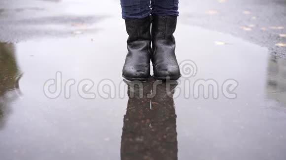 一个穿着黑色皮靴的女孩在雨中缓慢地在秋天的水坑里蹒跚而行视频的预览图