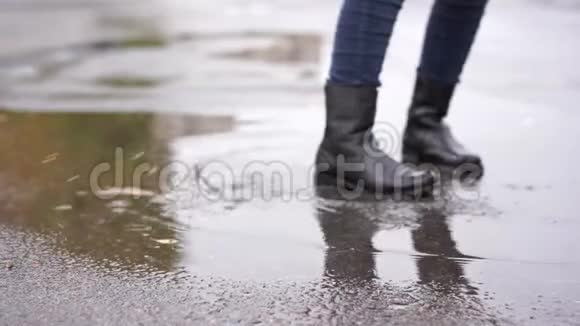 一个穿着黑色皮靴的女孩在雨中在秋天的水坑里跌倒视频的预览图