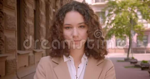 一位年轻的长头发卷曲的白种人女学生的特写镜头她正站在街上看着摄像机视频的预览图
