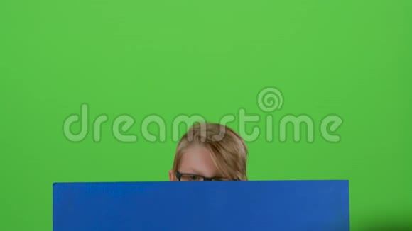 戴眼镜的小男孩从黑板后面走出来在绿色的屏幕上挥手视频的预览图