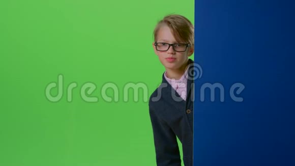 戴眼镜的少年从墙后出来在绿色的屏幕上显示舌头视频的预览图