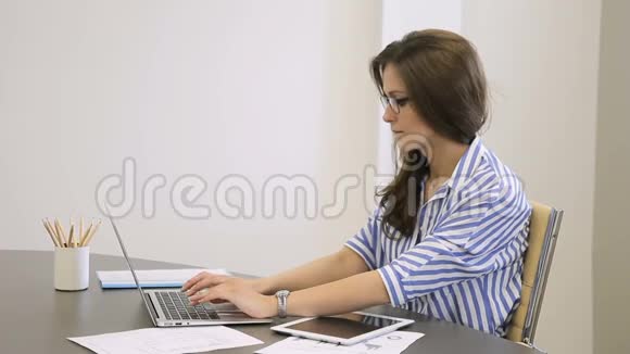 在现代办公室秘书使用笔记本电脑和平板电脑视频的预览图