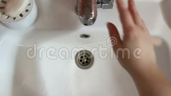 一个女人手冲洗牙刷然后涂上一层浆糊雌性的手在水流下与白色的贝壳相衬顶部视频的预览图