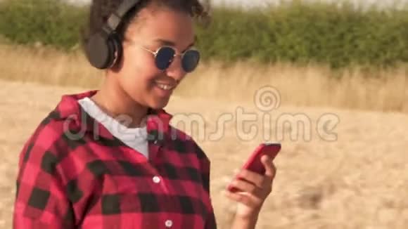 非洲裔美国少女戴着蓝色太阳镜走在无线耳机上听音乐的年轻女子视频的预览图