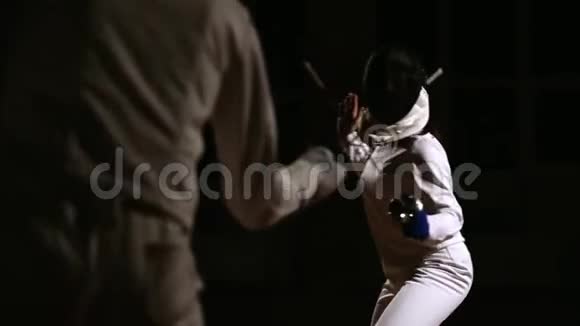 青年男女戴着帽子和西装做击剑用剑作战黑暗的背景击剑教练指挥一个视频的预览图