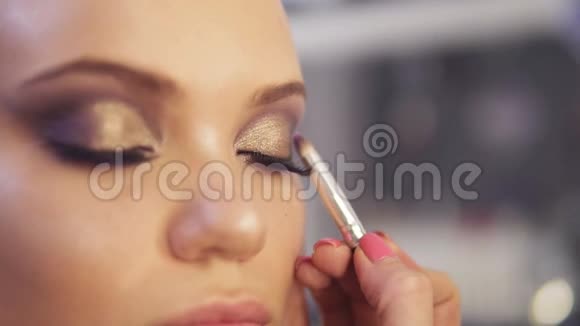 化妆师将金色眼影化妆应用于模特眼睛近景视频的预览图