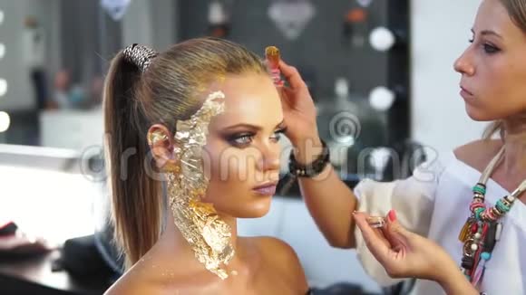 化妆师用特殊的刷子在模特头发上涂上金色的闪亮粉末准备时装表演视频的预览图
