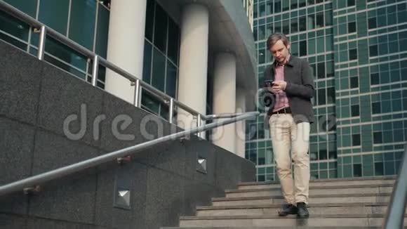 男人在电话里发短信休闲型城市职业创业者使用智能手机微笑办公大楼外视频的预览图
