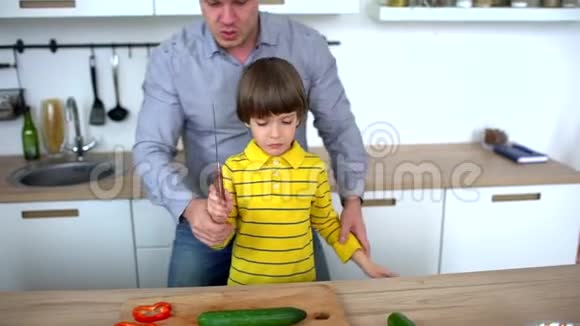年轻人和他的儿子在切黄瓜后一起在厨房拍手父子切菜视频的预览图