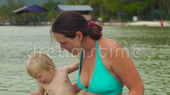 一个女人和她的小儿子在海滩上玩红色海星的慢镜头视频的预览图