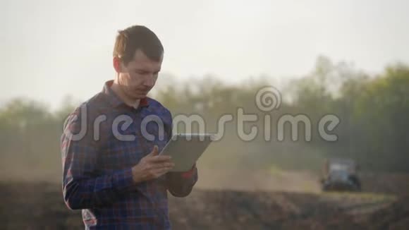 农民在耕地上使用数字平板电脑背景中的拖拉机概念现代技术视频的预览图