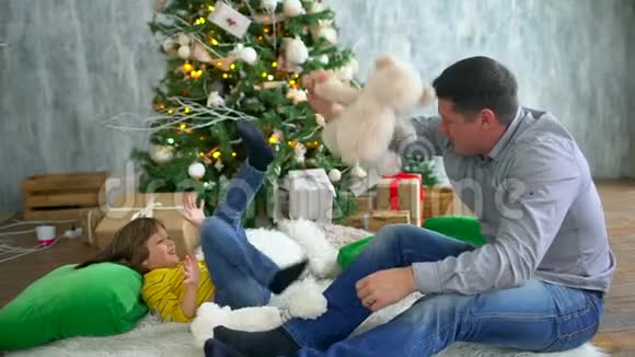 冬季圣诞家庭可爱的父亲和非常可爱的儿子在家中以圣诞树为背景玩得很开心视频的预览图