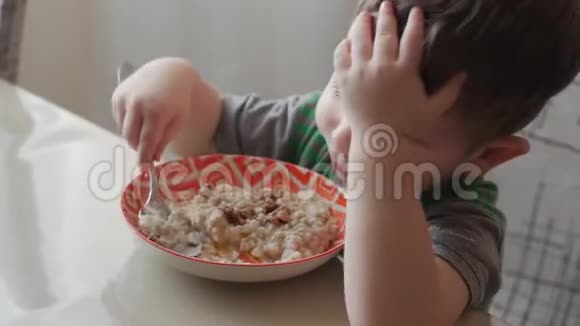 可爱的小宝宝一个人用勺子从盘子里吃粥健康饮食的概念视频的预览图