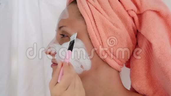 年轻女子用刷子在脸上缓慢地涂抹化妆品面膜女孩在她的脸颊上戴上面具女孩做的视频的预览图