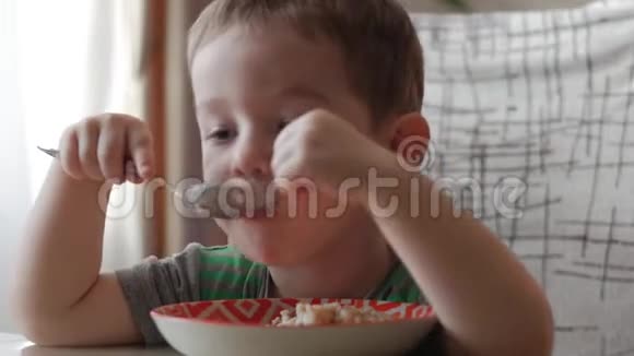可爱的小宝宝一个人用勺子从盘子里吃粥健康饮食的概念视频的预览图