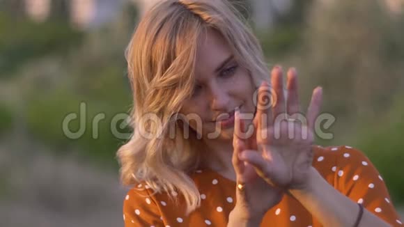 迷人的年轻女子双手带着金色的闪光在夕阳下的田野慢动作视频的预览图