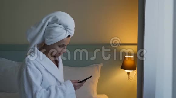 穿白色浴袍的年轻女子坐在酒店的床上视频的预览图