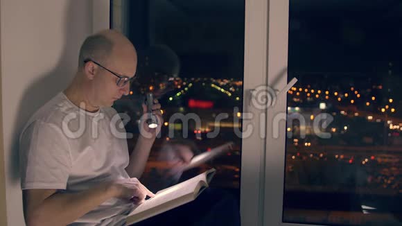 夜间坐在窗台上用手电筒看书的成年男子视频的预览图