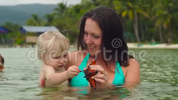 一个女人和她的小儿子在海滩上玩红色海星的慢镜头视频的预览图