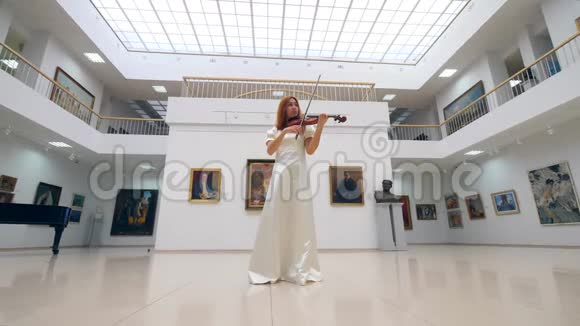 穿白色连衣裙的女士正在画廊大厅拉小提琴视频的预览图