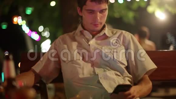 年轻的帅哥晚上在海滩咖啡馆里使用智能手机购物冲浪网络1920x1080视频的预览图