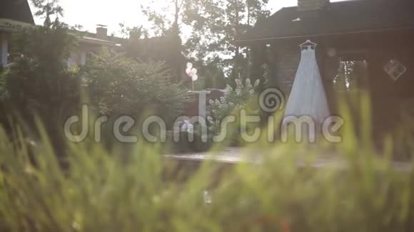在阳光下白色婚纱挂在靠近游泳池的房子的墙边视频的预览图