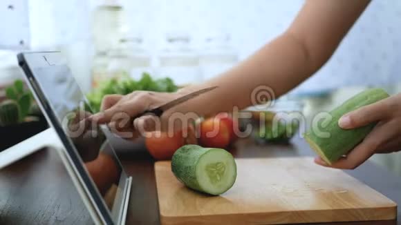 4K女人用手指滑在平板电脑上剥一根黄瓜准备烹饪原料然后在网上烹饪视频剪辑视频的预览图