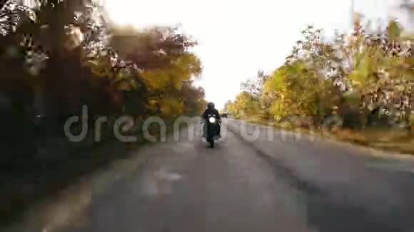 在阳光明媚的日子里一个身穿黑色头盔和皮夹克的男子骑着摩托车在马路上靠近视频的预览图