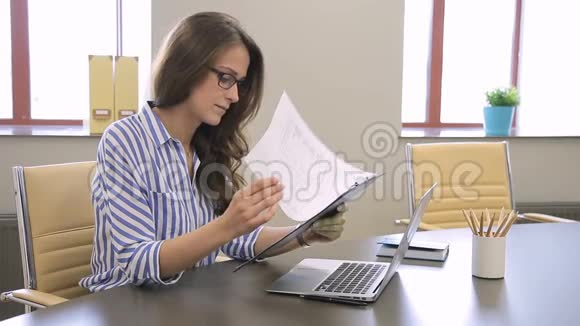 女员工正在看纸质文件并在笔记本电脑上键入文本视频的预览图